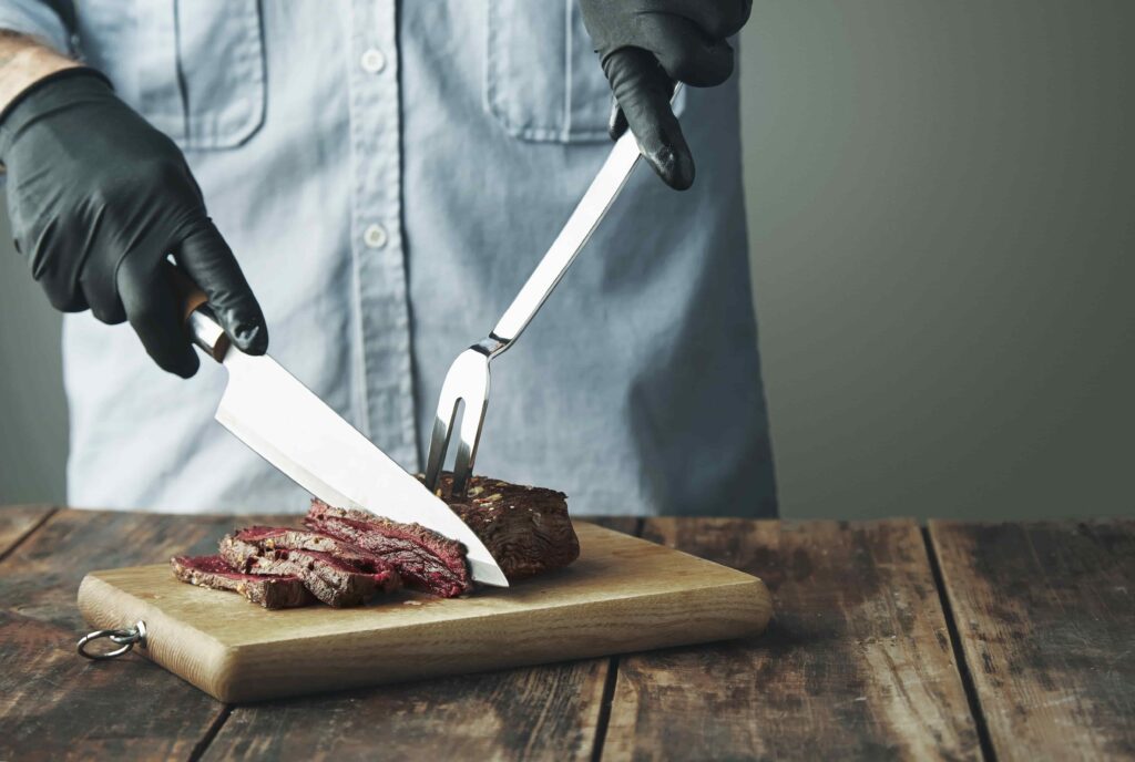 tattooed butcher hands black gloves with knife slice piece grilled meat wooden board min